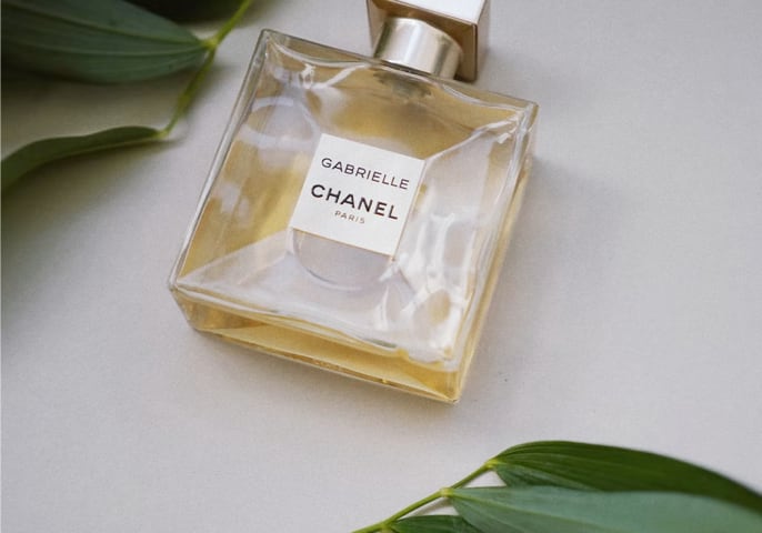  Gabrielle CHANEL perfume laying on a table surrounded by green leaves